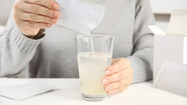 Person gibt eine Portion Glaubersalz in ein Glas mit Wasser