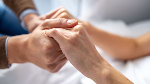 Person die an Leukämie stirbt hält die Hand von einem Angehörigen