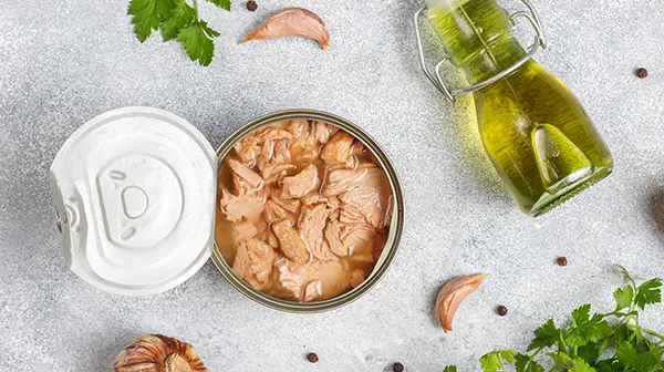 Dose mit Thunfisch, arrangiert mit frischen Zutaten wie Petersilie, Knoblauch und Olivenöl, was die sichere Zubereitung von Thunfisch in der Schwangerschaft symbolisiert.