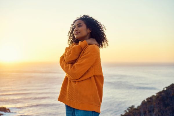 Eine junge Frau steht bei Sonnenuntergang an einer Küste