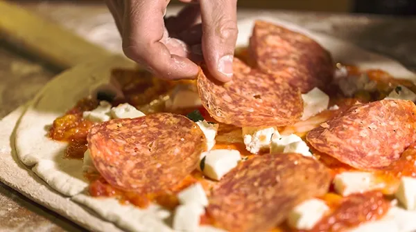 Eine Hand greift ein Stück aus einer Salamipizza